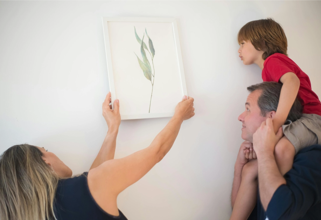Family hanging a framed artwork on the wall together.